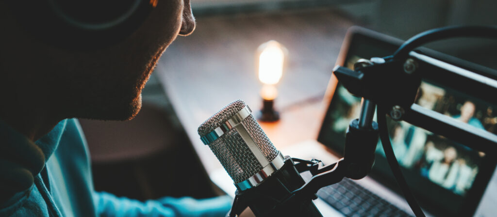 Young host streaming his live podcast using professional microphone at small broadcast studio